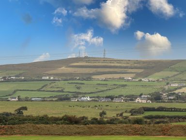 A rural landscape with fields, scattered houses, cows grazing, and a hill with transmission towers at Moybella Lodge in Lisselton near Ballybunion County Kerry