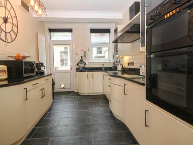 A kitchen with black countertops cream cabinets a wall clock microwave oven and a door at Morolwg in Llanaber near Barmouth