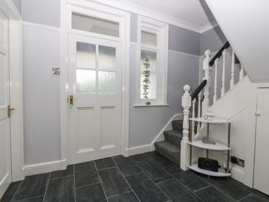 A hallway with grey tiled floor white doors a staircase with grey carpet and a small shelf under the stairs at Morolwg in Llanaber near Barmouth