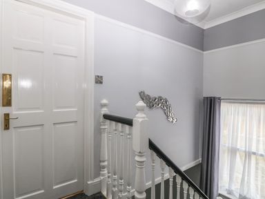 A stairway with white railing next to a closed white door and window with sheer curtains at Morolwg in Llanaber near Barmouth