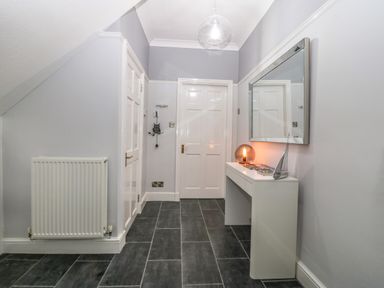 A hallway with two white doors a white radiator a white console table with a lamp and decorations and a rectangular mirror at Morolwg in Llanaber near Barmouth