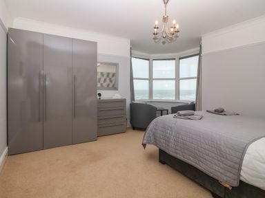 A bedroom with a bed and folded towels a wardrobe a chest of drawers two chairs and a table by a bay window at Morolwg in Llanaber near Barmouth