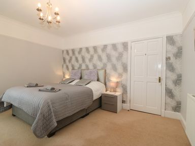 A bedroom with a bed two bedside tables with lamps a door and patterned wallpaper at Morolwg in Llanaber near Barmouth