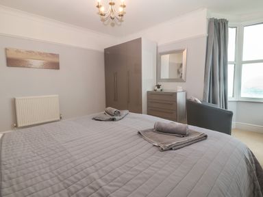 A bedroom with a bed towels wardrobe chest of drawers chair and window at Morolwg Llanaber near Barmouth