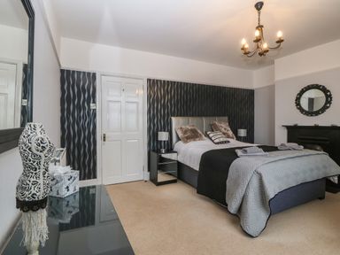 A bedroom with a bed bedside tables a black fireplace and patterned wallpaper at Morolwg in Llanaber near Barmouth