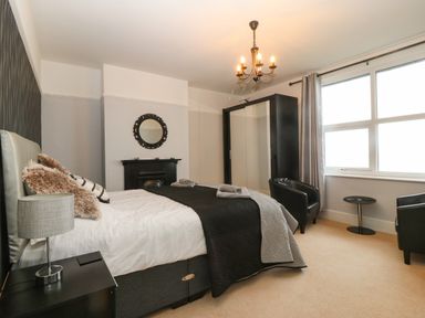 A bedroom with a bed side table and lamp two black chairs and a small round table by the window at Morolwg in Llanaber near Barmouth