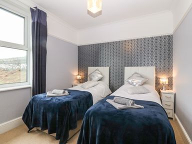 A bedroom with two single beds covered with dark blue blankets and white headboards at Morolwg in Llanaber near Barmouth