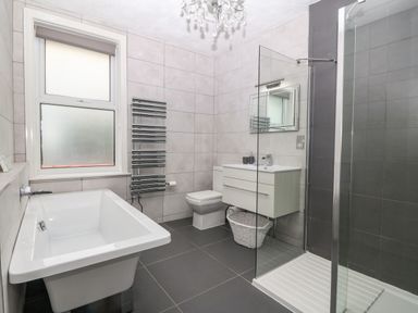 A bathroom with a bathtub, toilet, sink with cabinet, shower area, towel radiator, and frosted window at Morolwg in Llanaber near Barmouth