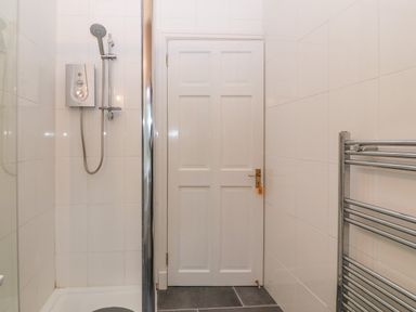 A bathroom with a shower unit a white door and a chrome heated towel rail at Morolwg in Llanaber near Barmouth