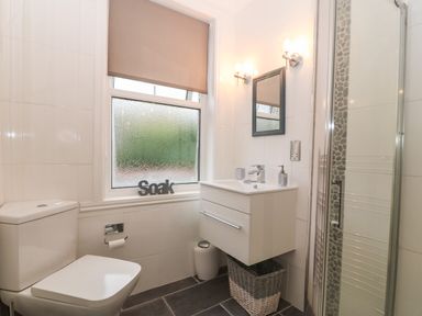 A bathroom with a toilet sink vanity mirror shower and window with a blind at Morolwg in Llanaber near Barmouth
