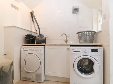 A utility room with a washing machine and dryer under a countertop with a sink and a laundry basket at Morolwg Llanaber near Barmouth