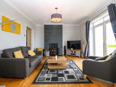 A living room with a gray sofa and armchair a wood burner and a TV at Morolwg in Llanaber near Barmouth
