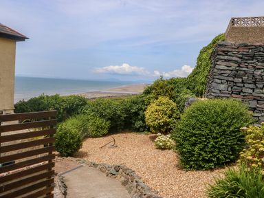 A garden with shrubs and gravel near a stone wall overlooking the beach and sea at Morolwg in Llanaber near Barmouth