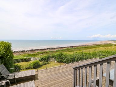 A wooden deck with lounge chairs overlooking a grassy area and a beach at Morolwg in Llanaber near Barmouth