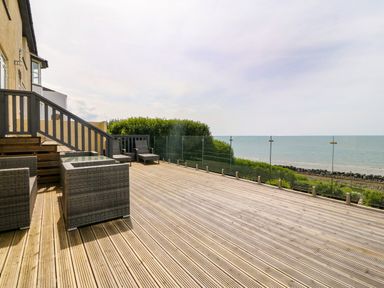 An outdoor wooden deck with wicker chairs and glass railing overlooking the sea at Morolwg in Llanaber near Barmouth