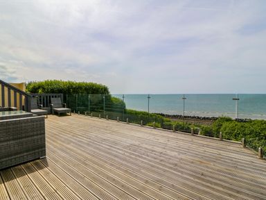 A wooden deck with lounge chairs and a glass railing overlooking the sea at Morolwg in Llanaber near Barmouth