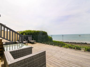 A wooden deck with outdoor wicker furniture and glass railing overlooking the sea at Morolwg in Llanaber near Barmouth