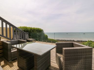 An outdoor deck with rattan furniture and glass railing overlooking the sea at Morolwg in Llanaber near Barmouth