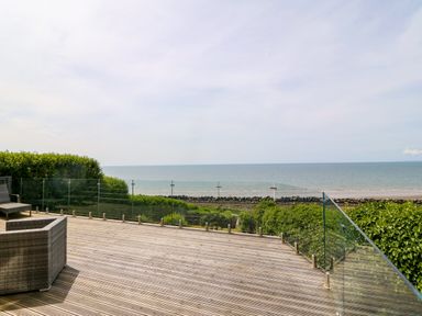 A wooden deck with glass railing overlooking the sea and greenery at Morolwg in Llanaber near Barmouth