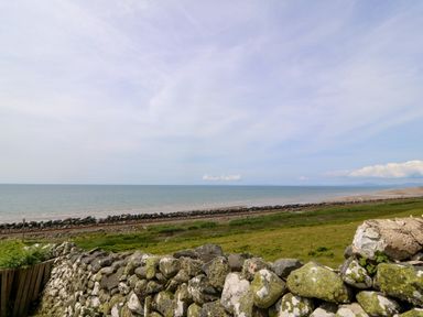 A coastal landscape with a stone wall green grass a railway track and the sea at Morolwg in Llanaber near Barmouth