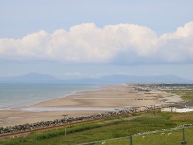 A beach with sand and water next to a rocky shoreline and grassy area at Morolwg in Llanaber near Barmouth