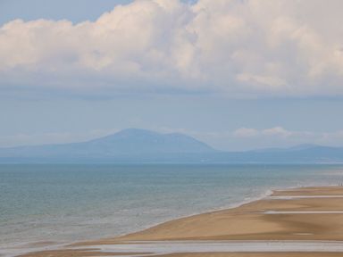 A beach with sand and shallow water and a mountain in the background at Morolwg in Llanaber near Barmouth