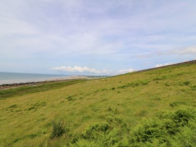 A grassy hillside overlooking a beach and sea with a fence along the hill at Morolwg in Llanaber near Barmouth