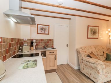 A kitchen area with stovetop toaster and sink next to a floral patterned sofa at Woods Edge in Mitcheldean