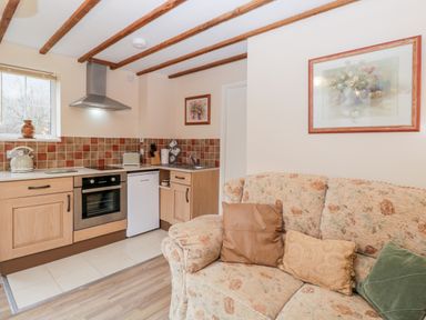 A kitchen with wooden cabinets a stove a small fridge and a floral sofa with cushions at Woods Edge in Mitcheldean