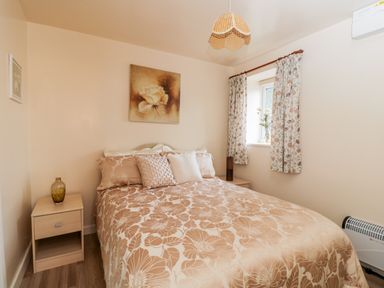 A bedroom with a double bed and floral bedding beside two wooden nightstands with a vase and a lamp at Woods Edge in Mitcheldean