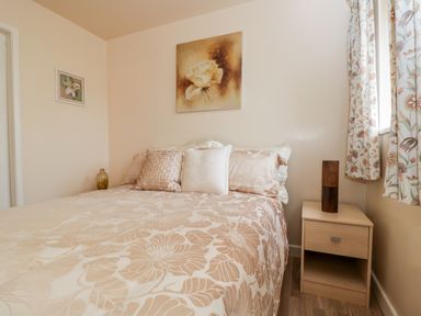 A bedroom with a bed with floral bedding pillows artwork on the wall a bedside table and patterned curtains at Woods Edge Mitcheldean