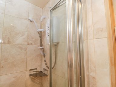 A tiled shower area with a white showerhead and a metal corner shelf at Woods Edge in Mitcheldean