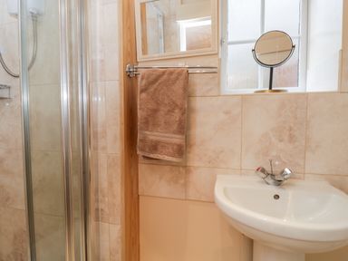 A bathroom with a shower enclosure a towel on a rack a sink with taps a mirror and a round table mirror on the window sill at Woods Edge in Mitcheldean