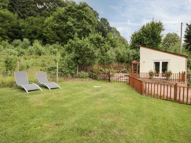 A garden with two lounge chairs a small fenced patio and a small building in a rural setting at Woods Edge in Mitcheldean