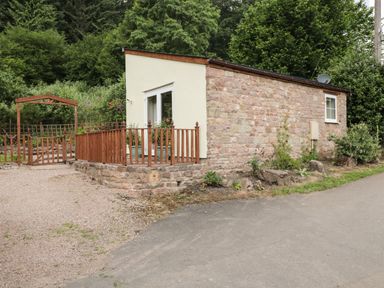 A small stone and plaster house with a wooden fence and garden gate surrounded by trees at Woods Edge in Mitcheldean