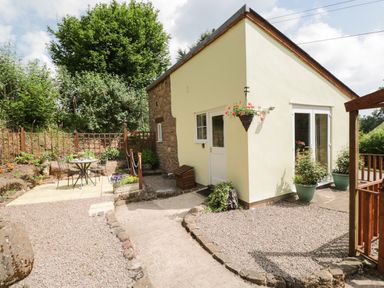 A small yellow house with a garden area and outdoor seating at Woods Edge in Mitcheldean