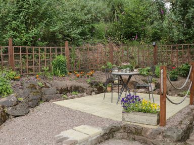 A garden patio with a round table and two chairs surrounded by plants and flowers at Woods Edge in Mitcheldean