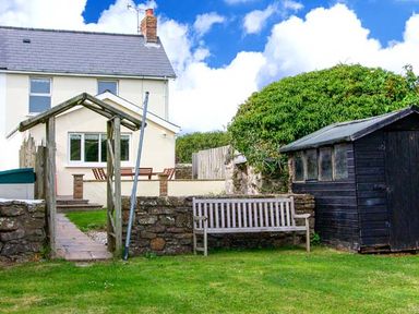 A garden with a wooden bench a black shed and a stone wall outside a white house at The Grange in Little Haven near Haverfordwest