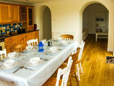 A dining table set with plates and bowls in a kitchen with wooden cabinets and two archways at The Grange in Little Haven near Haverfordwest 