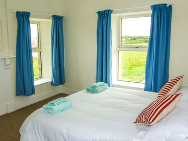 A bedroom with a bed with striped pillows blue curtains and folded towels on the bed at The Grange in Little Haven near Haverfordwest