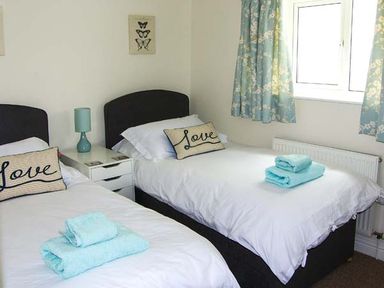 A bedroom with two single beds with love pillows and folded towels on the beds a bedside table with a lamp and floral curtains at The Grange in Little Haven near Haverfordwest