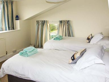 A bedroom with two single beds with white linens and turquoise towels near a window with striped curtains at The Grange in Little Haven near Haverfordwest 