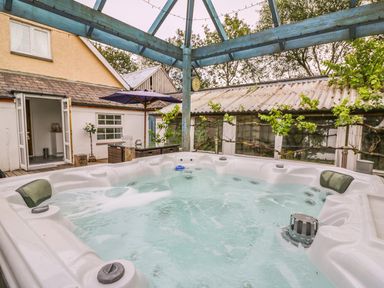 An outdoor hot tub with bubbling water under a wooden canopy near a house and patio furniture at Cariad Cottage in Cross Inn