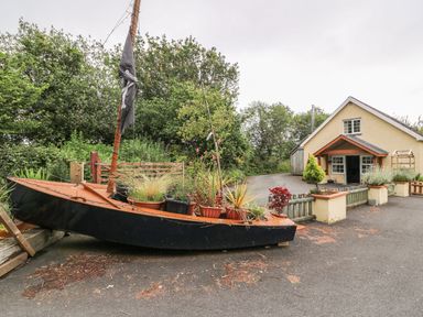 A small boat filled with plants beside a driveway next to a house at Cariad Cottage in Cross Inn