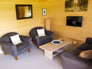 A sitting area with two armchairs a sofa a coffee table and a wall-mounted television at Pennylands Willow Lodge in Broadway