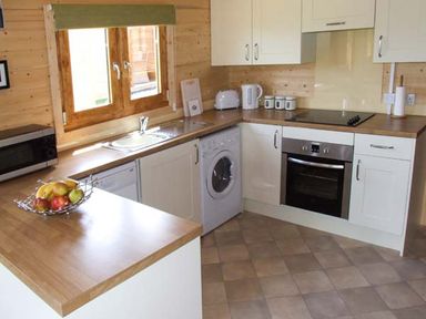 A kitchen with white cabinets wood countertops a window a sink an oven a washing machine and a fruit bowl at Pennylands Willow Lodge Broadway