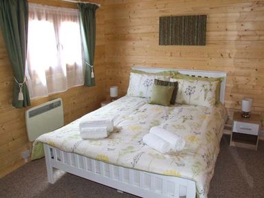 A bedroom with a white bed with floral bedding and towels on it beside a window with green curtains at Pennylands Willow Lodge in Broadway