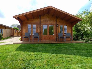 A wooden cabin with four chairs on the porch and a green lawn in front at Pennylands Willow Lodge in Broadway
