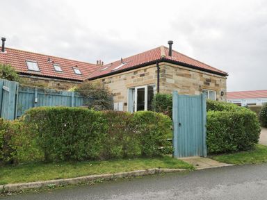 A corner stone house with a red tiled roof and blue wooden fence with green hedges at Mallard Cottage in Whitby