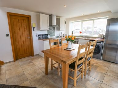 A kitchen with wooden table and chairs a vase with flowers microwave oven washing machine and refrigerator at Mallard Cottage in Whitby